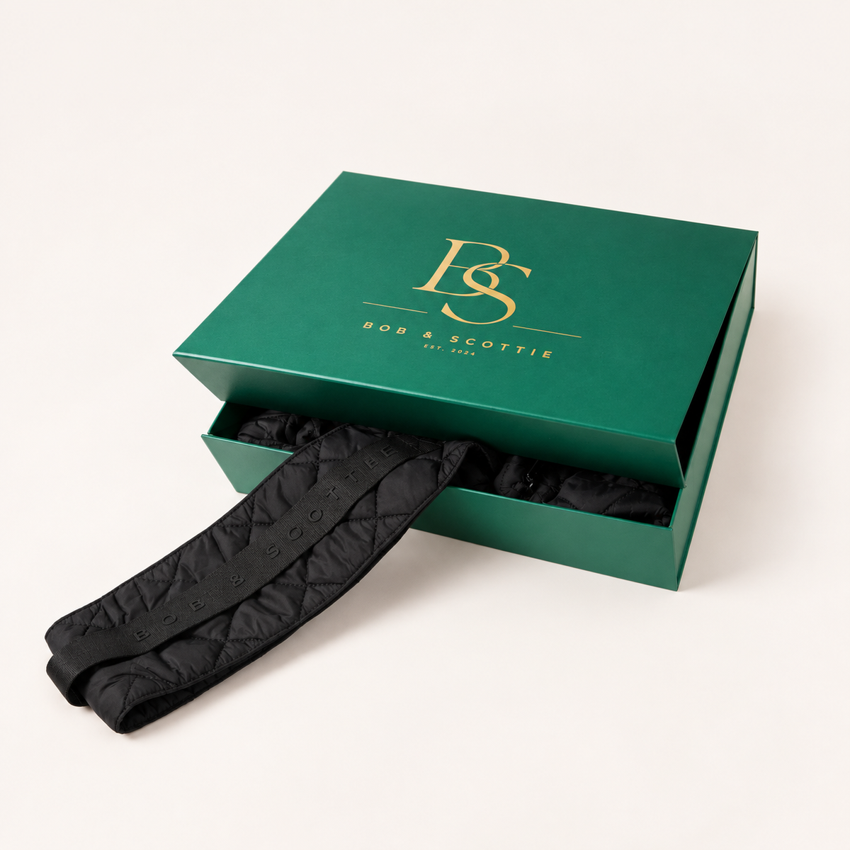 Gesloten groene geschenkdoos met gouden BS-monogram naast The Bob Carrier in zwart