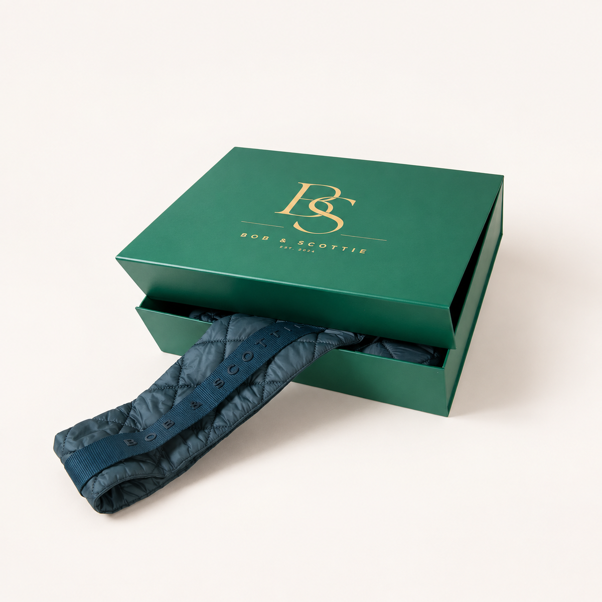 Gesloten groene geschenkdoos met gouden BS-monogram naast The Bob Carrier in petrol
