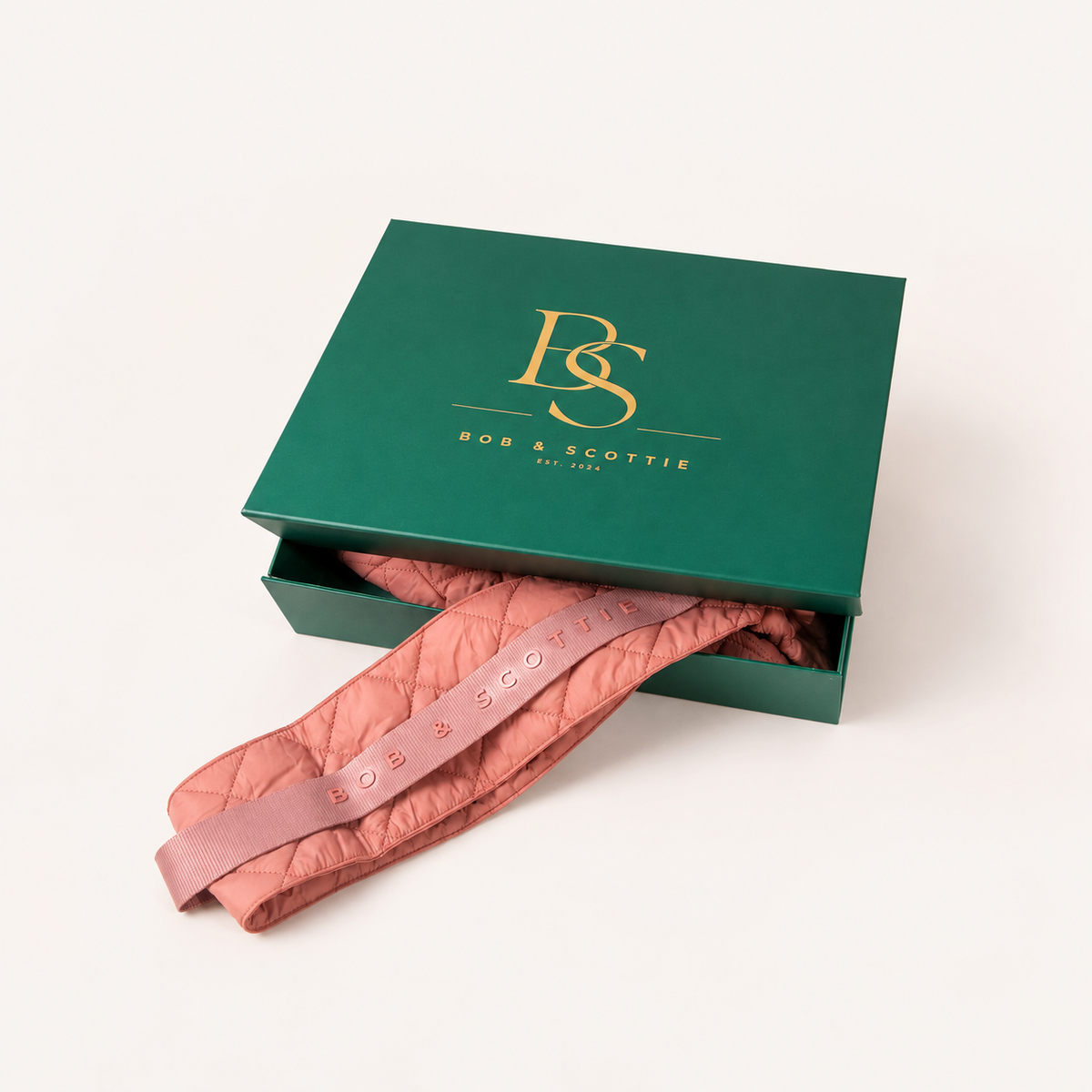Gesloten groene geschenkdoos met gouden BS-monogram naast The Bob Carrier in roze